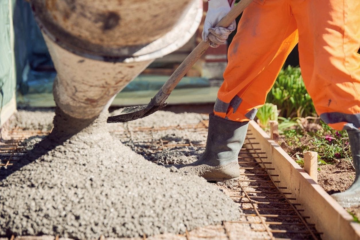 Worker spreading concrete with a shovel.
